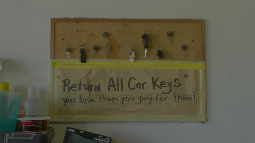 Board on a wall containing keys with a sign below them