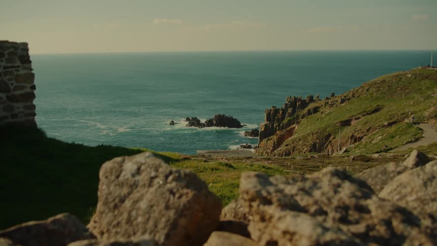 Rocky coastline with green cliffs extends into the ocean beneath an open horizon