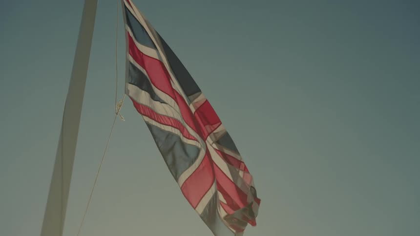 A united kingdom flag waves from a white pole against a clear blue sky during the day