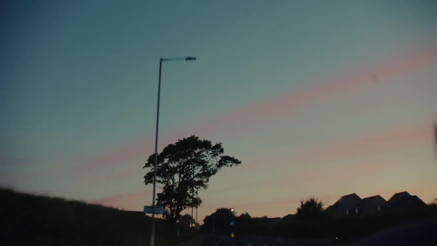 Car travels on a highway passing a residential area after dusk