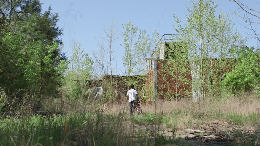 Person sitting on their bicycle while looking at a structure in a weed-filled field on a clear day