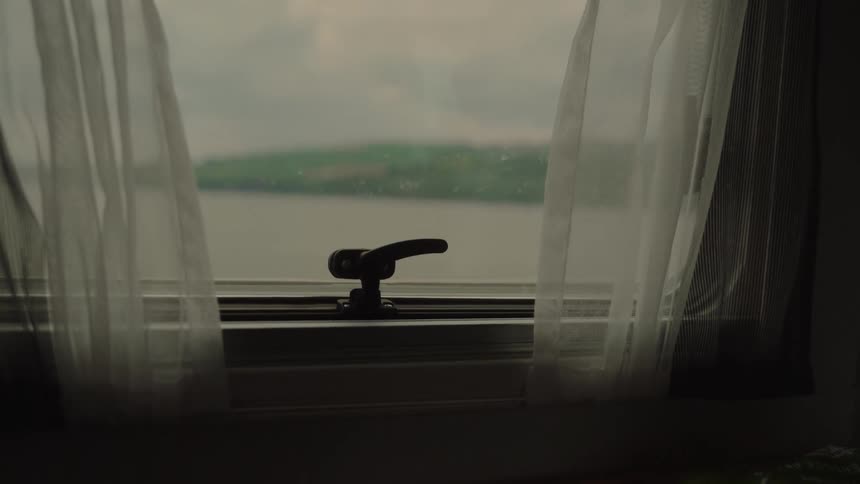 Window with sheer curtains frames a view of a lake and distant hillside