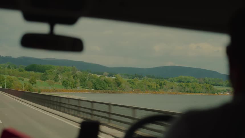 A man rides in a car that is passing by a large body of water