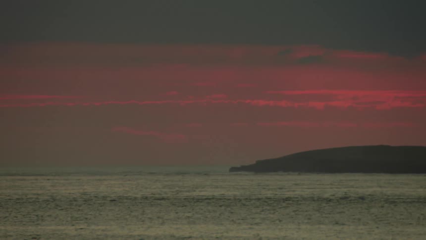 An ocean view from the coastline with an orange evening sky as the wind creates ripples on the water