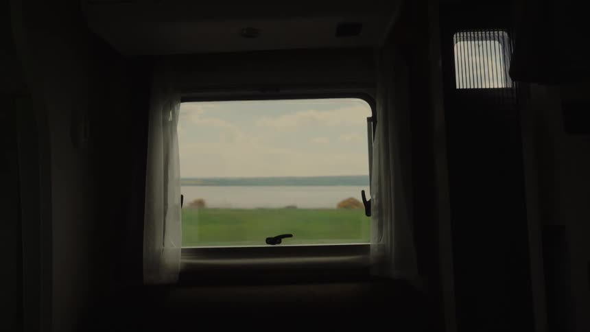 Vehicle window frames a landscape with a green field and a lake in the background