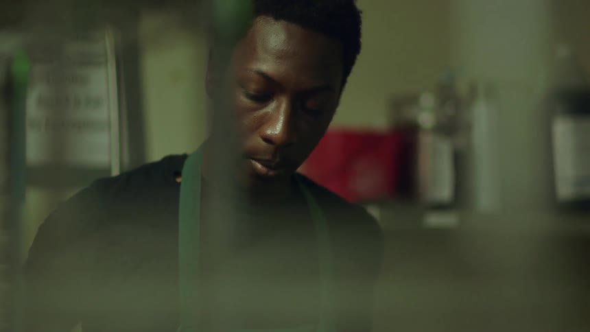 A young man in an apron stands still while looking around in a work environment
