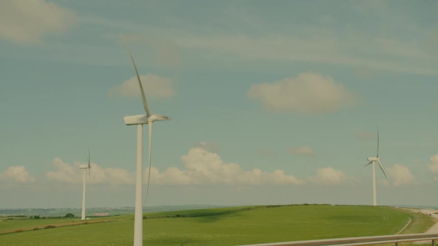 Wind turbines on a green hill under a cloudy sky