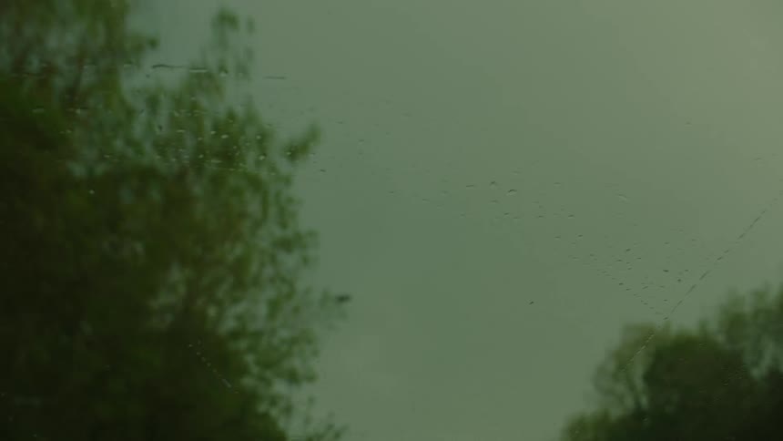 Rain pours on the windshield of the driving car