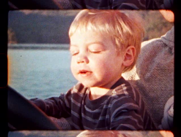Blond boy sitting on a boat with water in the background