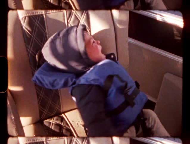 A young child wearing a blue winter jacket and hood sits in a car seat appearing to cry and have a temper tantrum