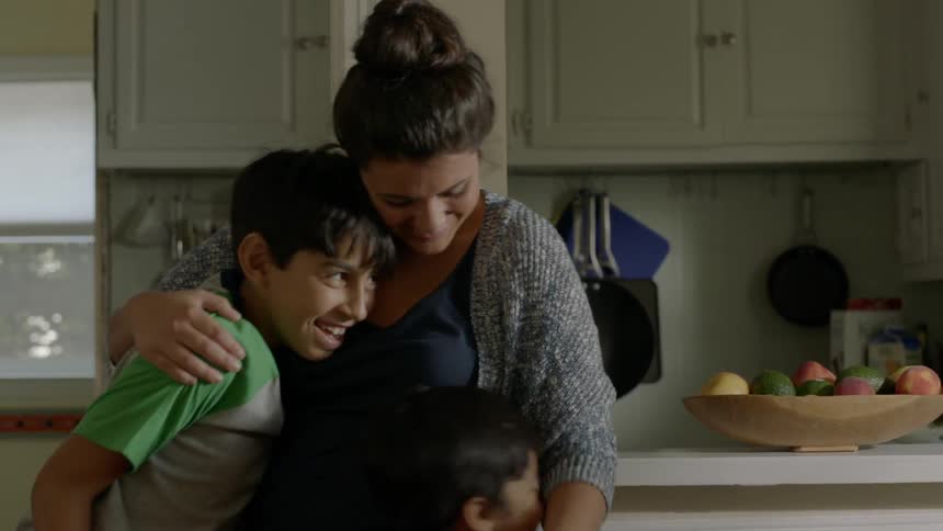 A woman hugs two boys in a kitchen