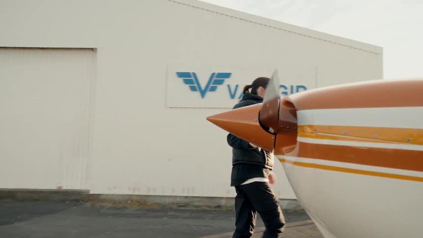 Person inspecting the propeller of a small airplane in front of a hangar