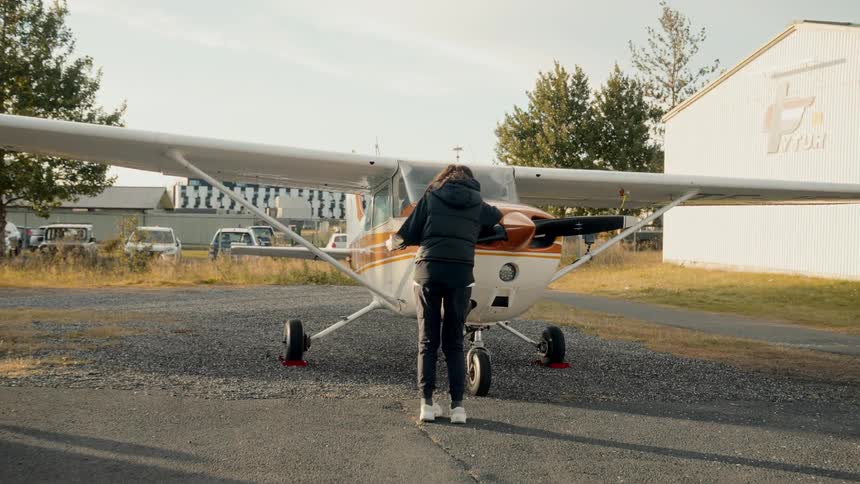 Woman approaches a small plane and stops to inspect the propeller on an autumn day