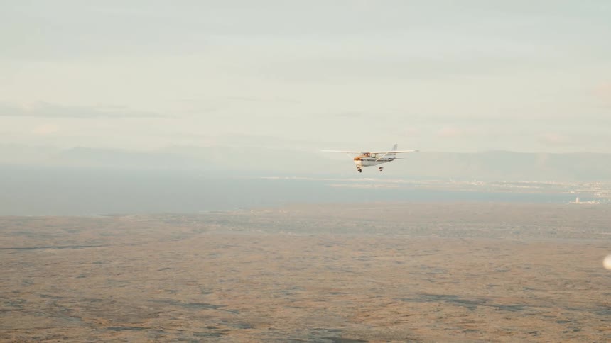 A small propeller plane flies low over a vast arid landscape with mountains in the distance