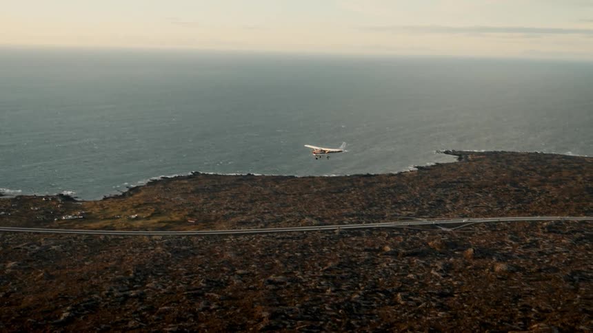 Singleengine airplane flies over a rocky coastline with the ocean in the background