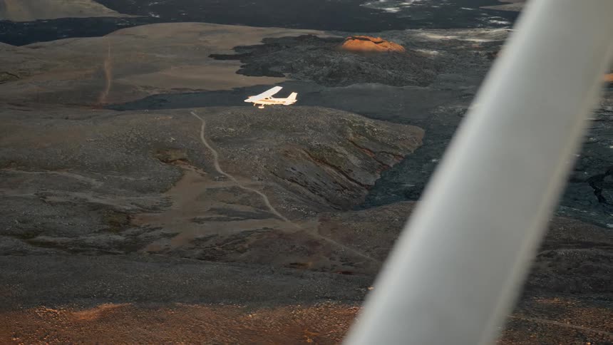 Small airplane flying over a rural road in the mountains