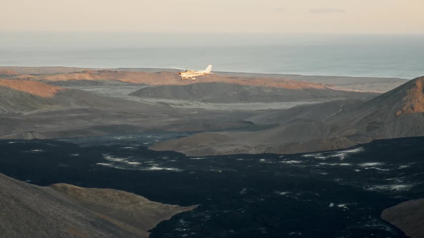 Airplane flying over a valley surrounded by mountains outdoors during dusk or dawn