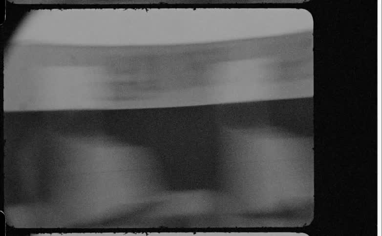 A view of a black and white film reel spinning quickly on a projector with visible grain and dust particles on the frames