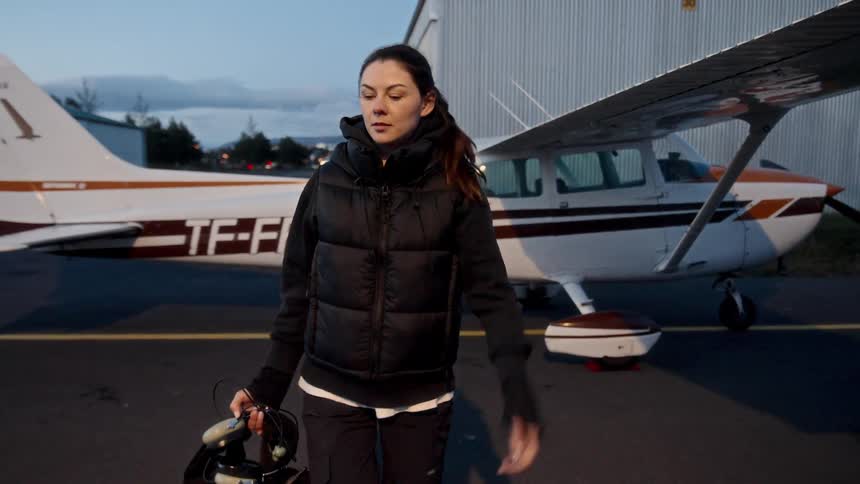 Young adult woman closing a door on an airplane then walking away through an airfield outdoors during dusk or dawn