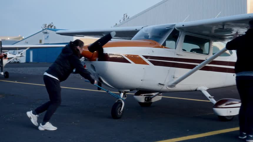 Two people are pushing a small plane backwards