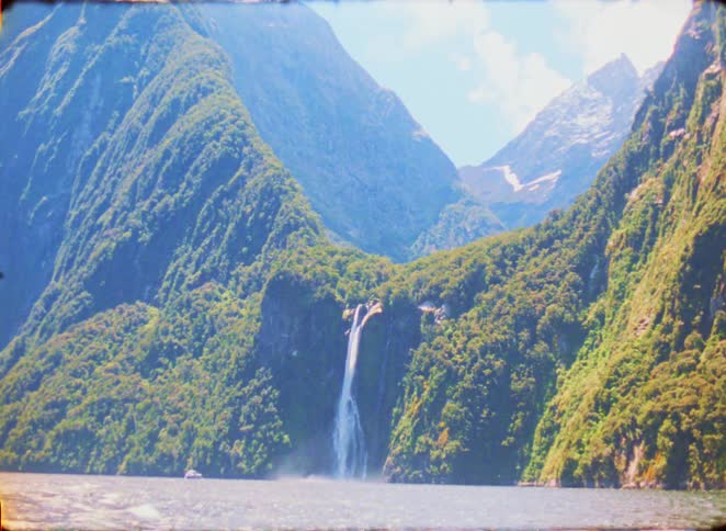 A tall waterfall flows over a mountain cliff into a large body of water