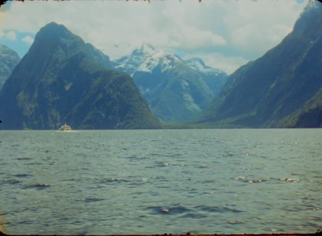 Boat sails on a lake surrounded by mountains with snowcapped peaks