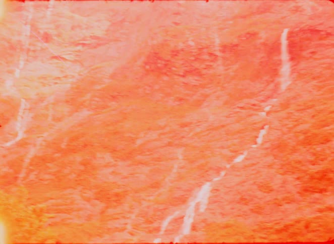 A view of a steep mountain face with many thin waterfalls cascading down the rocky surface during the day