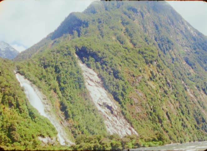A mountain with a stream flowing along its side surrounded by grasscovered terrain at midday