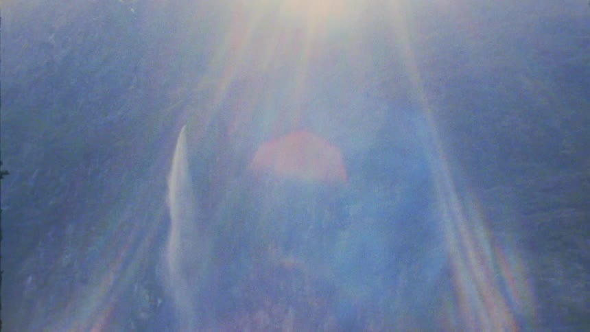 Glacial waterfalls cascade down rocky mountain cliffs under bright lens flares