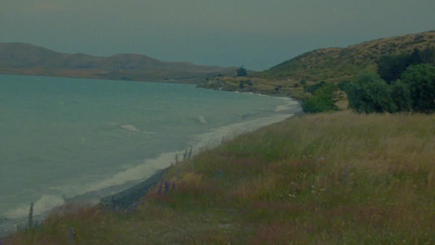The shoreline which creates a winding boundary where the turquoise water meets the dark pebbly beach