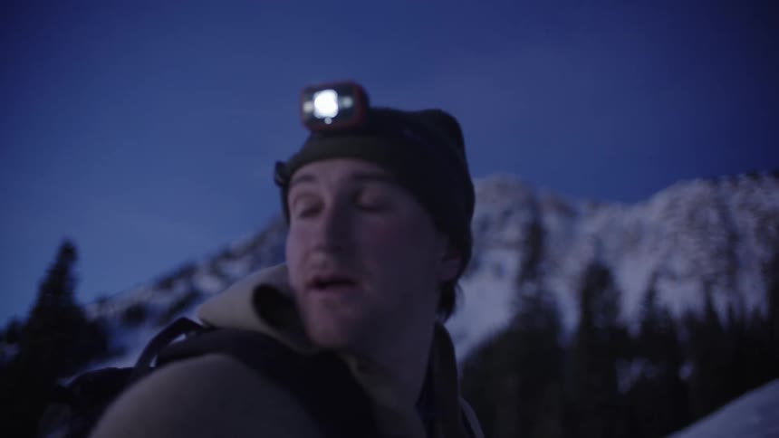 A young man hiking on a snowcovered mountain at evening wearing a headlamp and a jacket