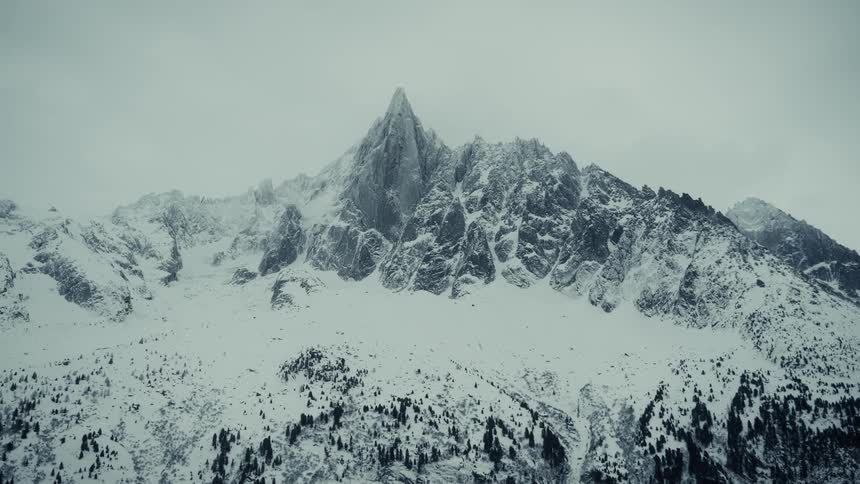 Snow and ice cover the rough terrain of mountains with peaks high in the cloudy winter sky