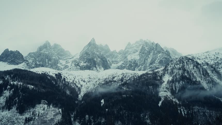 Snow and ice cover the rough terrain of mountains with peaks high in the cloudy winter sky
