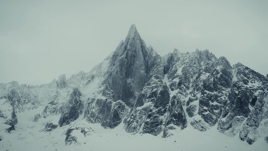 Snow covered mountain range with peaks high in the cloudy winter sky