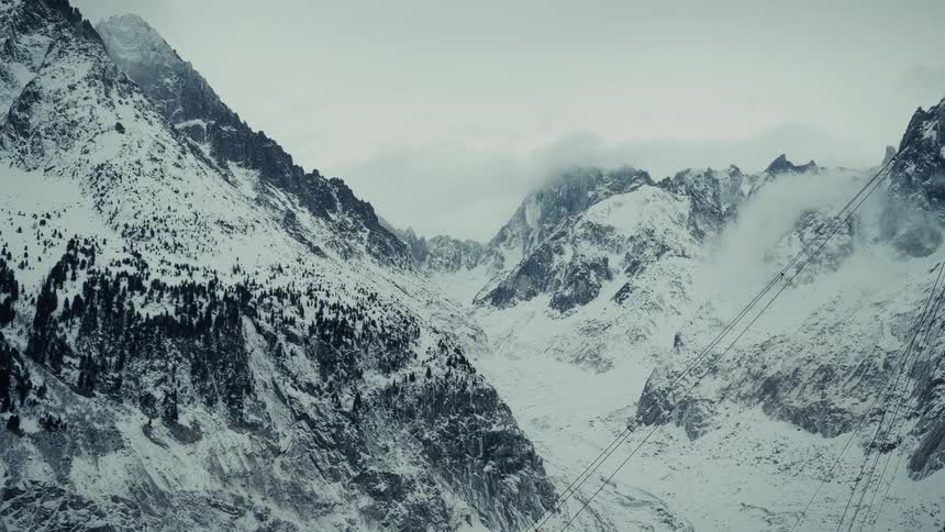 Snowcovered mountains with cables crossing the valley under a cloudy sky