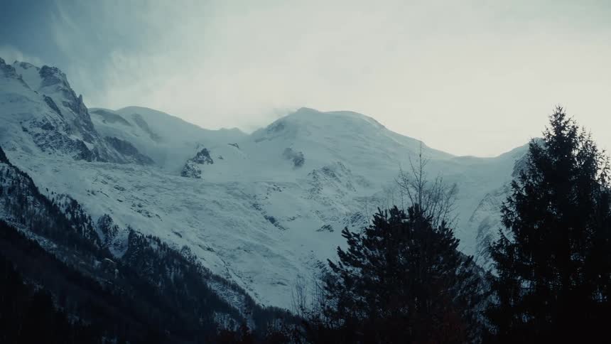 During winter on a highland with mountains covered in snow and trees growing along the mountain slopes at midday