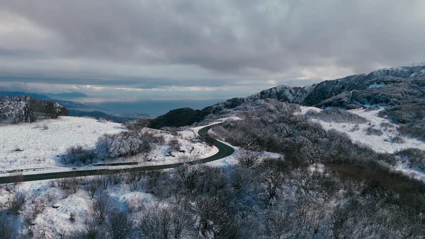 A winding road snakes its way across a hilly landscape covered in show