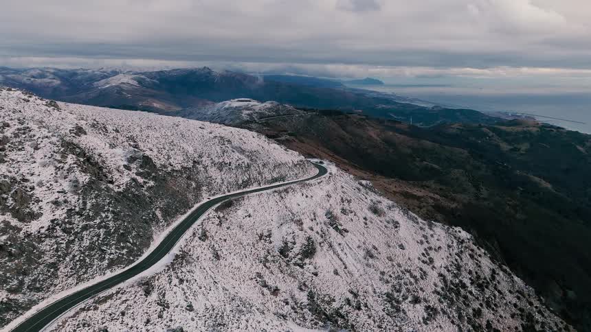 Cars travel on a road winding around snow covered mountains