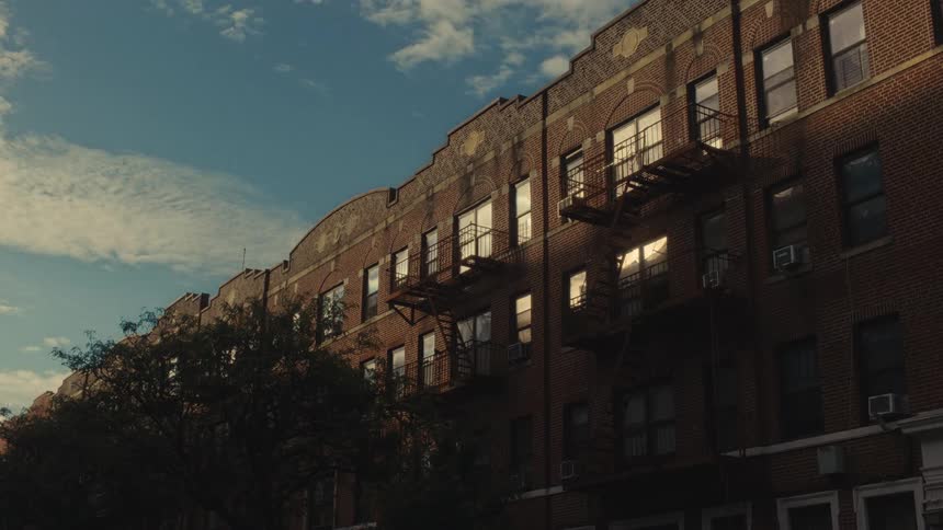 Brick residential building with metal fire escapes and symmetrical windows lit by sunlight