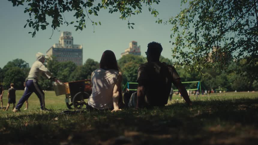 Two people sitting on grass watching activities in urban park
