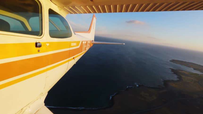 Singleengine airplane flies over a coastline with sea and strip of land at sunset