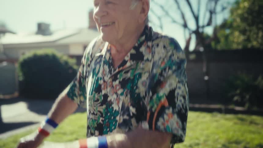 Elderly man wearing a sports headband and colorful wristbands moves his arms in the backyard