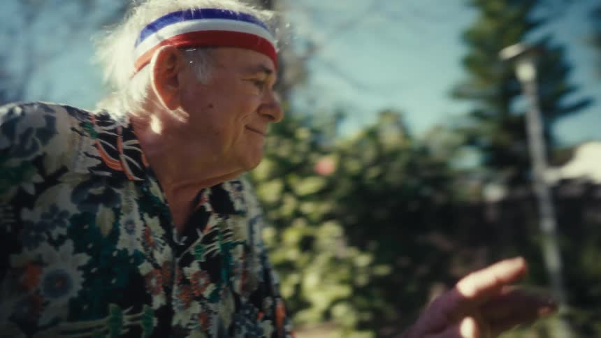 Elderly man wearing a sports headband dances in a house backyard