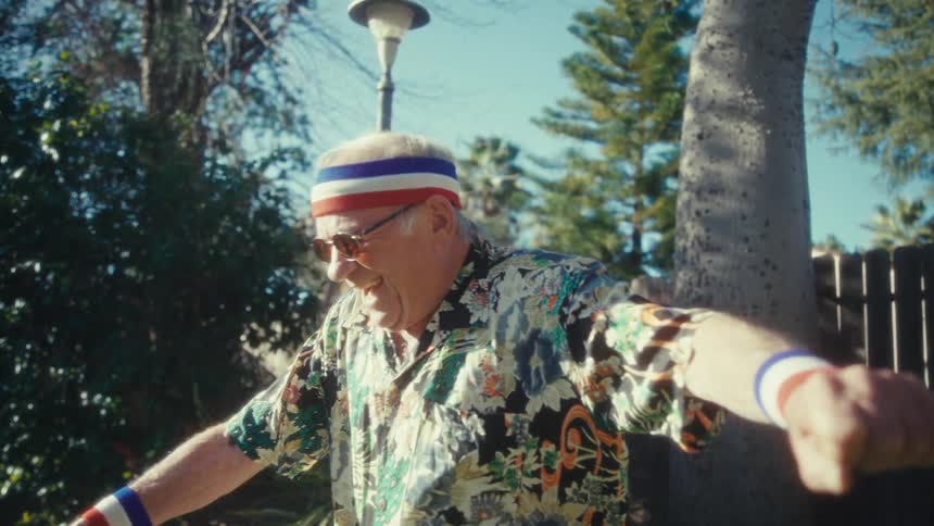 Man holds a leaf blower while dancing on the lawn wearing kneehigh socks and white sneakers