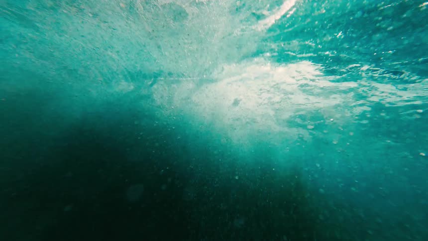 Bubbles and light pass through blue water seen from below the surface