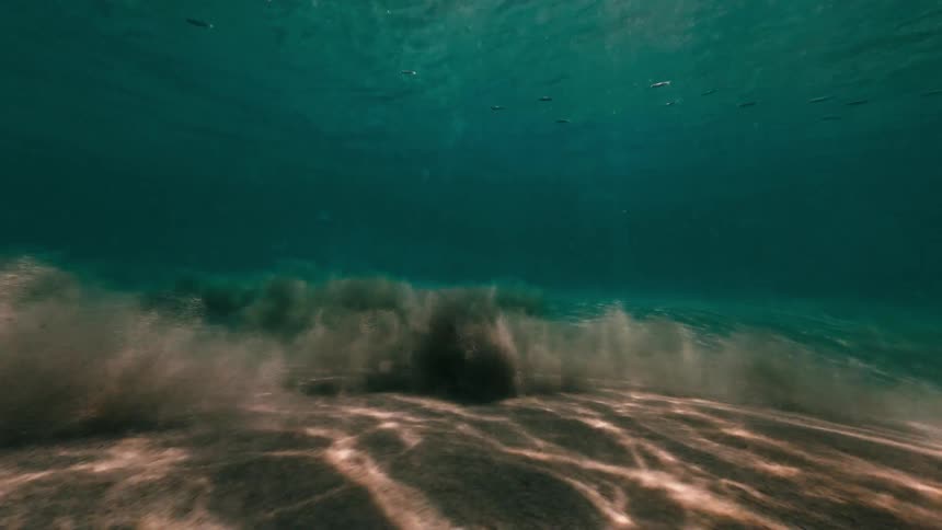 Sunlight filters through turquoise ocean water while sand kicks up below