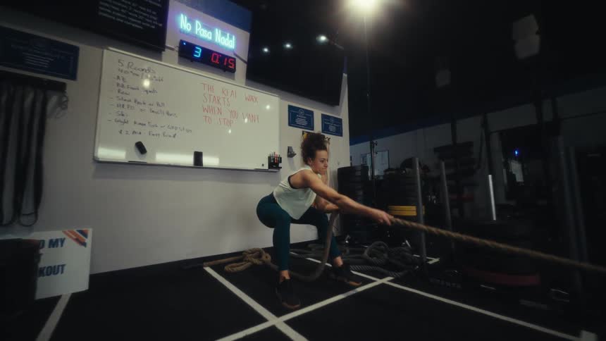A woman in a gym vigorously pulls a rope as part of her exercise