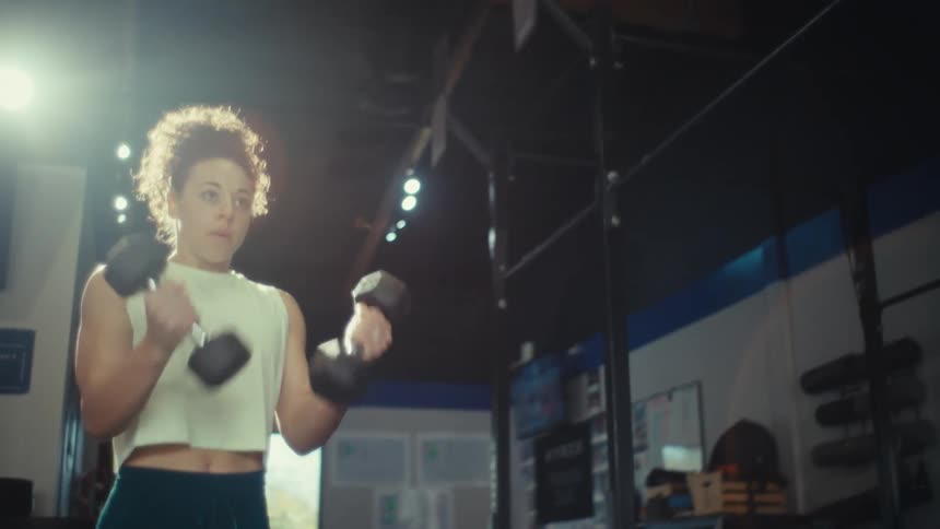 A young woman carrying dumbbells in the gym during her exercise session at midday