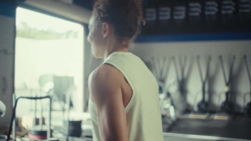 The woman lifts barbells while looking outside the gym