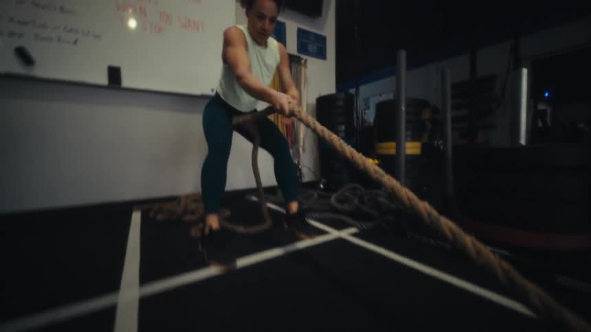 A young woman in the gym dragging a rope weight during an intense workout